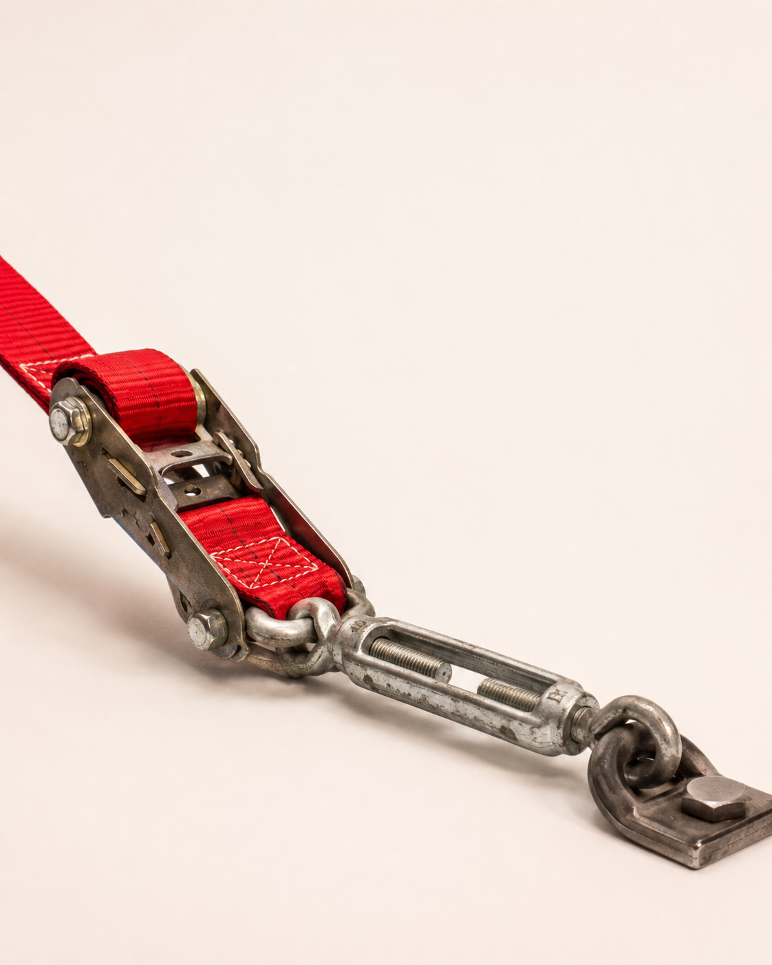 A heavy-duty red ratchet strap connected to a metal turnbuckle and lashing anchor point used for cargo securing.