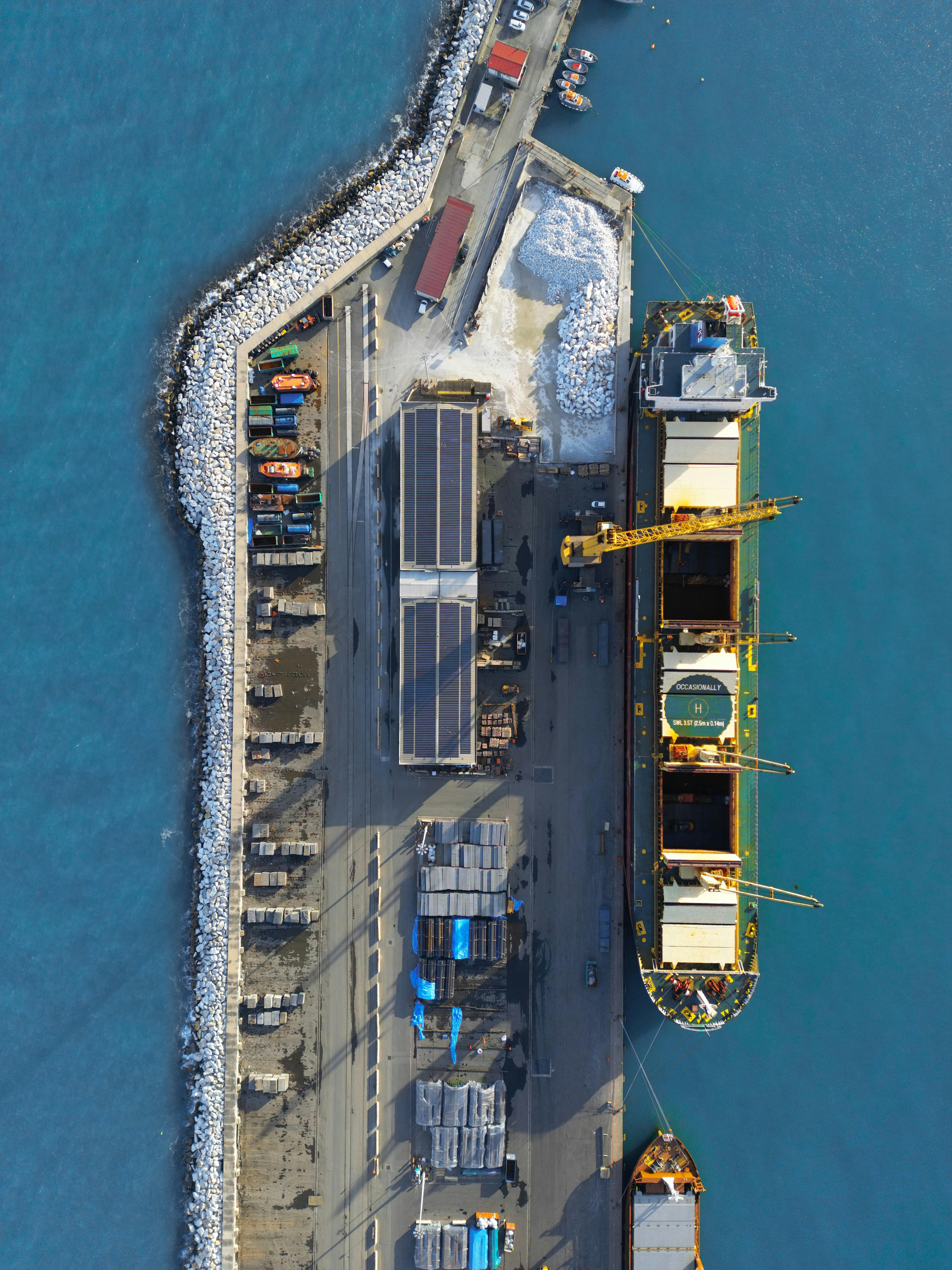 Top-down aerial view of a general cargo ship docked at a port terminal handling breakbulk goods and raw materials.